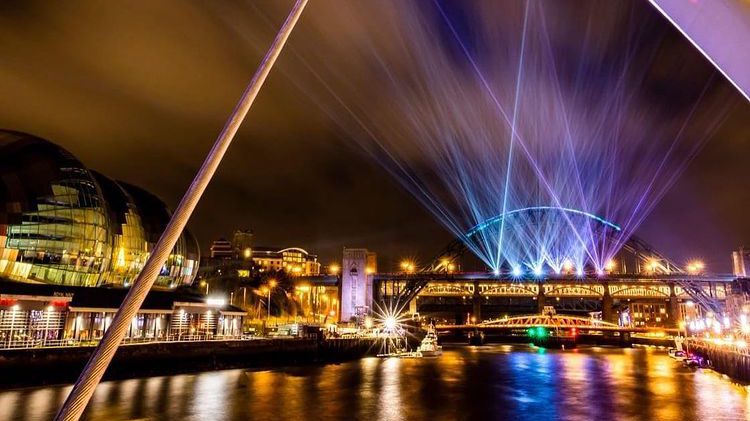Laser beams on the Tyne Bridge at night, reflecting off the water